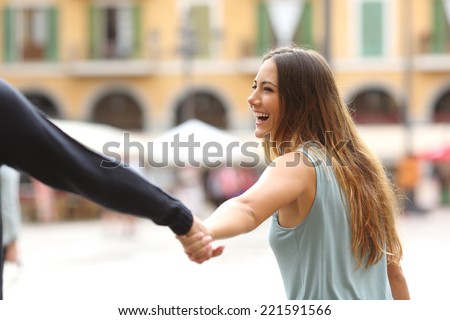 Happy tourist woman laughing and pulling her boyfriend in a touristic place