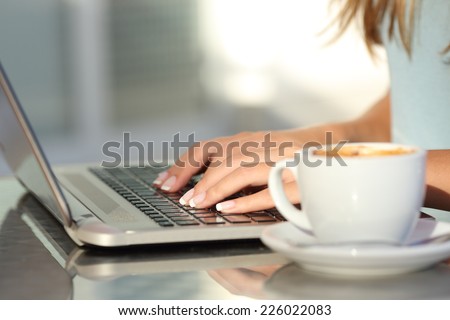 Close up of a woman hands typing in a laptop in a coffee shop terrace in the street