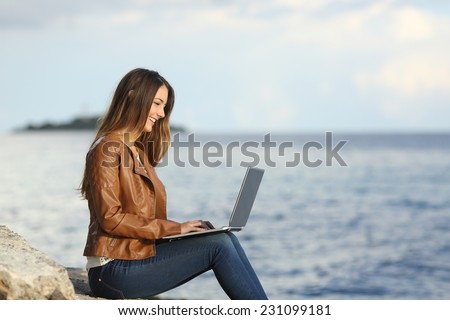 Profile of a self employed woman working with a laptop on the beach with the sea in the background