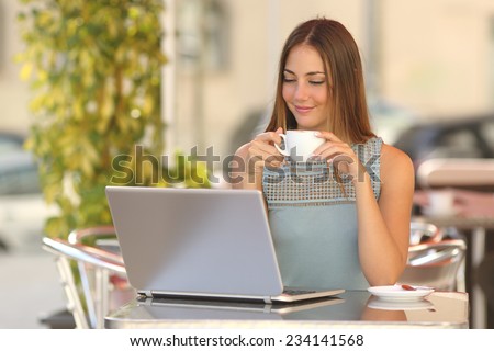 Relaxed woman watching a laptop in a restaurant and holding a cup of coffee