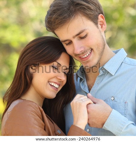 Couple hugging and holding hands while looks an engagement ring outdoors