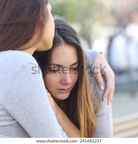 Sad girl crying and a friend comforting her outdoors in a park