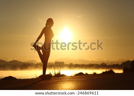 Silhouette of a fitness woman profile stretching at sunrise with the sun in the background