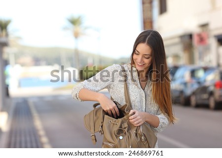Casual happy woman walking on the street and searching something in a bag