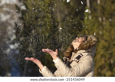 Happy girl throwing snow in the air on winter holidays in a forest in a sunny day