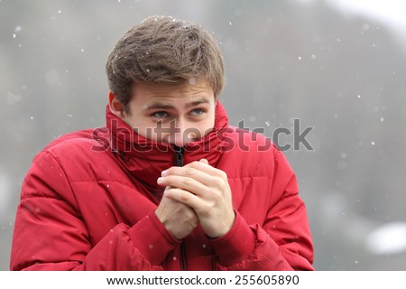 Man shivering in cold winter and rubbing hands while is snowing