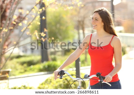 Candid woman walking in an urban park in summer or spring carrying a bicycle