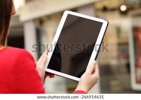 Woman using and showing a blank tablet screen in the street in front a store