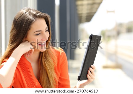 Happy woman reading a Tablet or ebook in a train station while is waiting for public transport