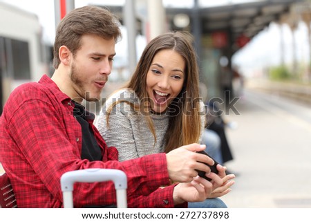 Funny couple playing games with a smart phone in a train station while they are waiting