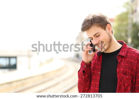 Traveler teen guy calling on the mobile phone in a train station while he is waiting
