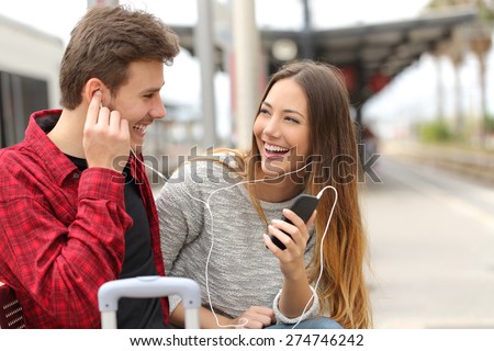 Happy couple of travelers sharing music on holidays during a travel in a train station