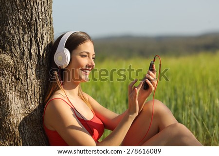 Girl listening to the music and downloading songs sitting in a green field wearing a red shirt