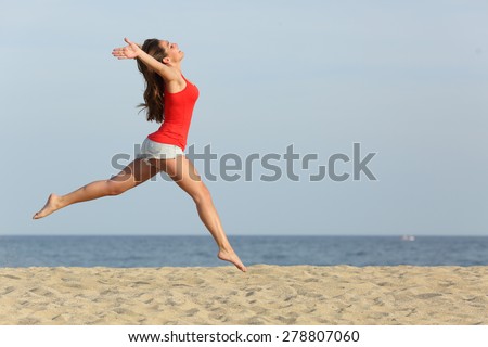 Side view, of a teen girl wearing red shirt and shorts jumping happy on the beach