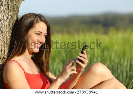 Girl texting in a smart phone relaxed in the country with a green field in the background