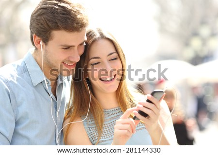 Happy couple with earphones sharing music from a smart phone on the street