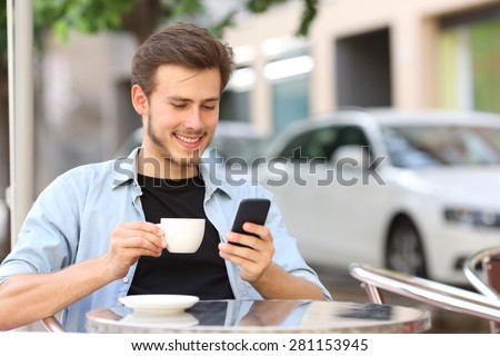 Man using a smart phone in a coffee shop sitting in the terrace outdoor and holding a cup