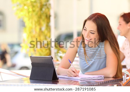 Happy student studying and learning taking notes with a digital tablet in a coffee shop