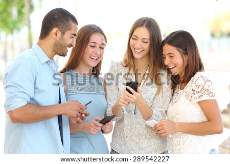 Four friends laughing happy and watching social media in a smart phone in the street every one with his own phone