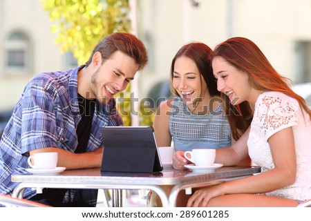 Three happy friends watching tv or social media in a tablet in a coffee shop terrace