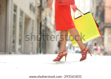 Side view of a shopper woman legs walking with shopping bags in a commercial street