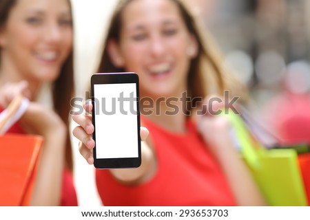 Two joyful shoppers with shopping bags showing a blank smart phone screen in the street