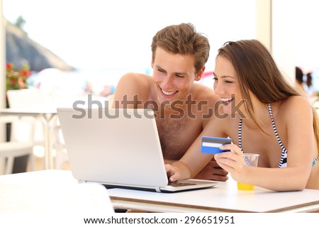 Couple buying online on holidays with a laptop and credit card on the beach