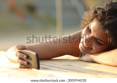 Girl watching videos or social media in a smart phone relaxing in a park at sunset