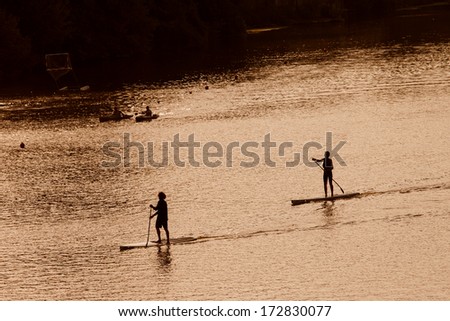 Silhouette of men paddleboarding at sunset, Florence river, Italy, recreation sport paddling ocean beach surf