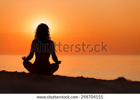 Silhouette of woman in yoga lotus meditation position front to seaside on sunrise