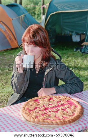 The young girl with red hair drinks tea near to a pie in tourist camp
