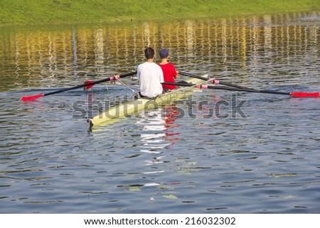 Two rowers in a boat, paddles on the tranquil lake