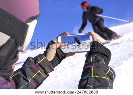 A young girl by cell phone photographed of skiers