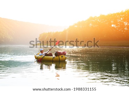 Tourist on yellow packraft rubber boat with red padle on a sunrise river. Packrafting. Active lifestile concept Stock fotó © 