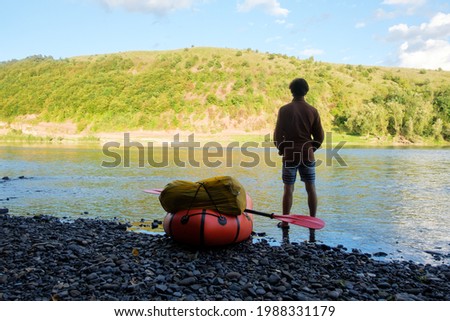 Tourist near yellow packraft rubber boat ready for adventures with red padle on a sunrise river. Packrafting. Active lifestile concept Stock fotó © 