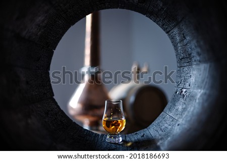 A glass of whiskey in old oak barrel. Copper alambic on background. Traditional alcohol distillery concept