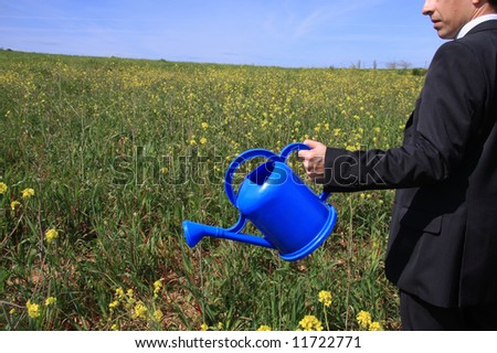 Detail of a business man with a blue watering can in a field