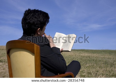 Business man reading a book on the meadow (text book with intentional blur)