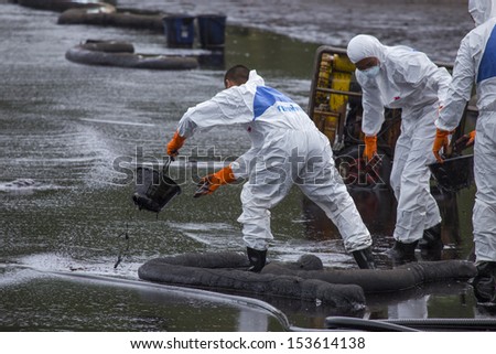 RAYONG, THAILAND - JULY 31, 2013: Workers wearing biohazard suits scoop a pail full of spilled crude oil as cleaning operations from a beach of Samet Island on July 31, 2013 in Rayong, Thailand.