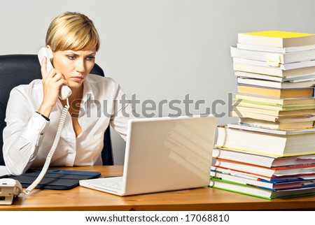 Young beautiful business lady working at a busy desk, speaking by phone.