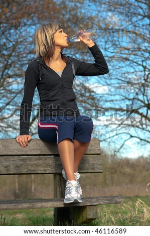 Sportswoman drinking water on a bench in a park.