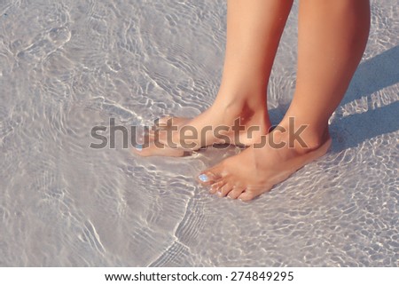 Female feet in water on the beach, white sand