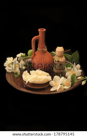 pitcher of clay, handmade oil,  facial cream and a sprig of jasmine flowers on a black background