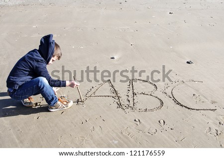 child writing the alphabet on beach sand