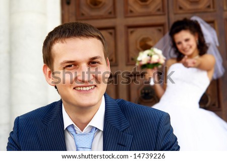 Smiling bridegroom is sitting near the church. His bride inviting him inside.