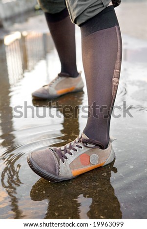 Girl in gym shoes is standing in the puddle.