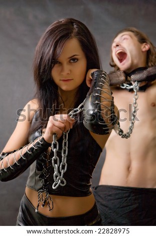 Pretty woman in leather clothing is holding a wired slave.
