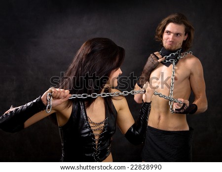 Pretty woman in leather clothing is holding a wired slave.