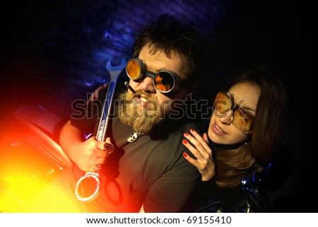 Crazy mechanic with the big wrench is looking at fire. Pretty girl embracing him.