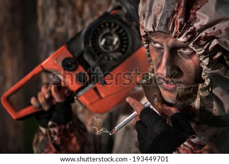 Smoking maniac with the chainsaw dressed in a dirty bloody raincoat. Focus on eyes and cigarette.
